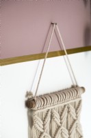 Detail of macrame hanging from nail on pink painted wall