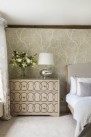 Flowers and lamp on chest of drawers in classic bedroom