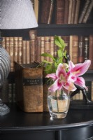Detail of cut lilies in glass of water next to old books