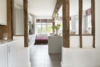 View through exposed wooden beams to white country kitchen