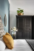 Bedroom with upholstered headboard, duck blue feature wall and black cupboard