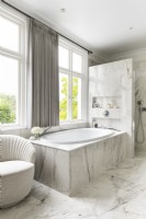 Classic, contemporary marble bathroom with bath by window and shower. 