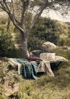 Vintage camp bed with cushions and blankets in woodland garden